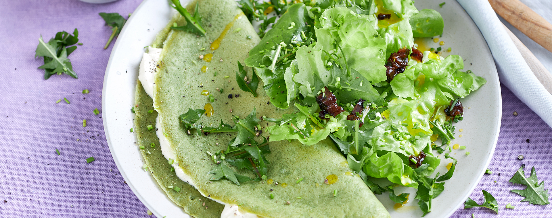 Brennnesselpfannkuchen mit Fetacreme-Füllung, bestreut mit Löwenzahnblättern, dazu ein grüner Salat mit Eichblattsalat und Löwenzahn.