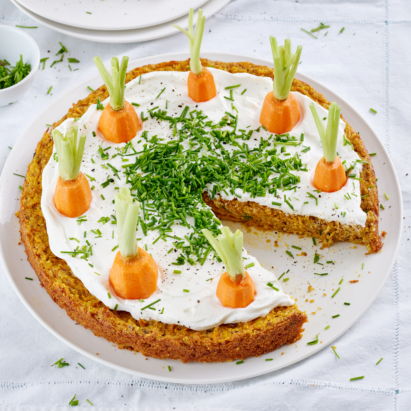 Herzhafter Möhrenkuchen mit Schnittlauchquark-Frosting auf einer Servierplatte.