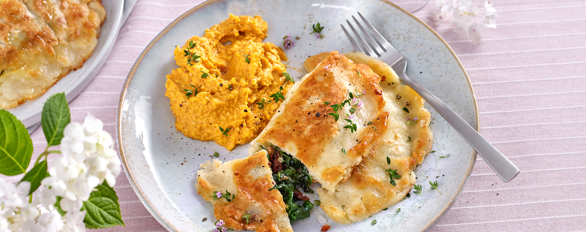 Kartoffel-Calzone mit Spinatfüllung und Möhren-Walnuss-Creme auf einem Teller.