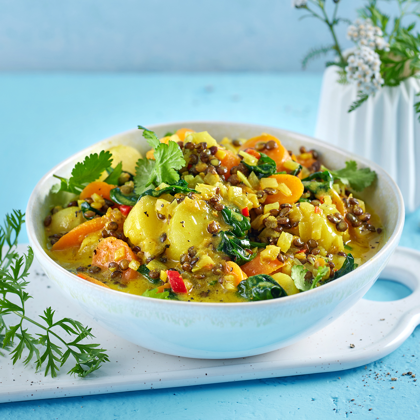 Möhrencurry mit Linsen und Kartoffeln in einer Schale, garniert mit frischem Koriander.