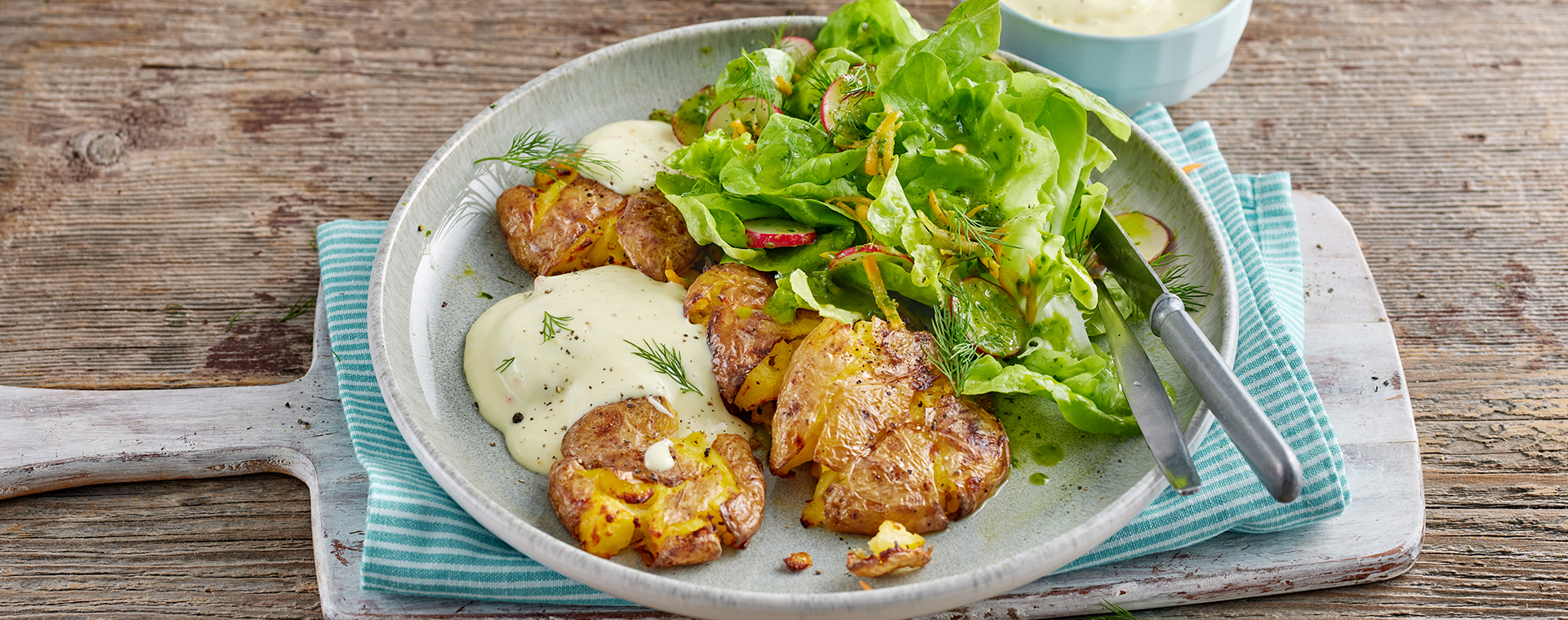 Quetschkartoffeln mit cremiger Soße à la hollandaise und Frühlingssalat, angerichtet auf einem Teller.