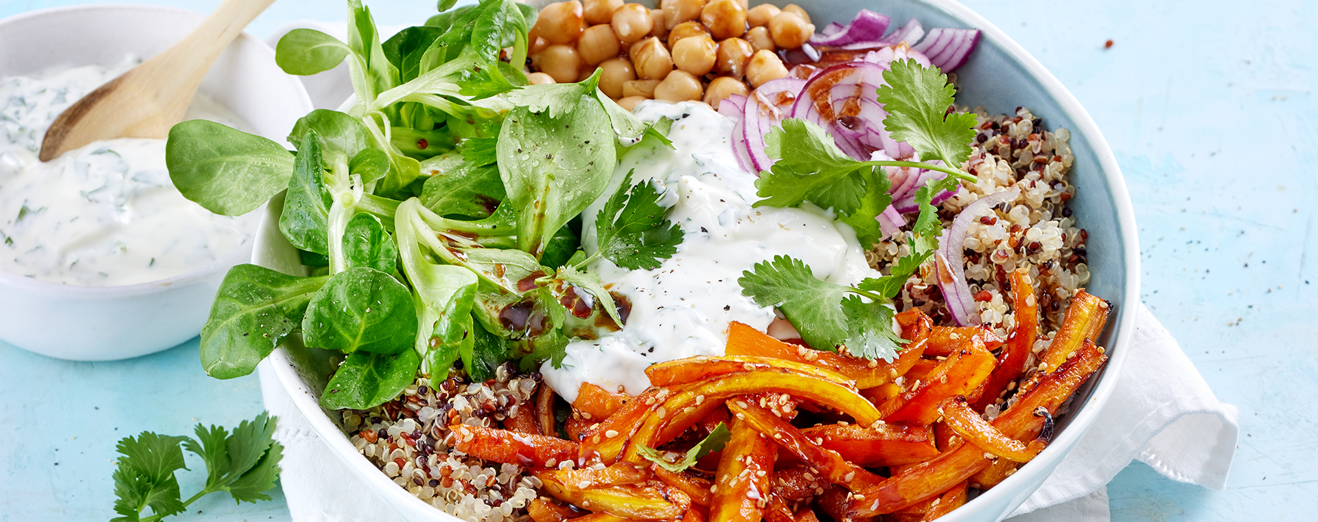 Quinoa-Bowl mit glasierten Möhrensticks und Joghurtsoße, garniert mit frischem Koriander.