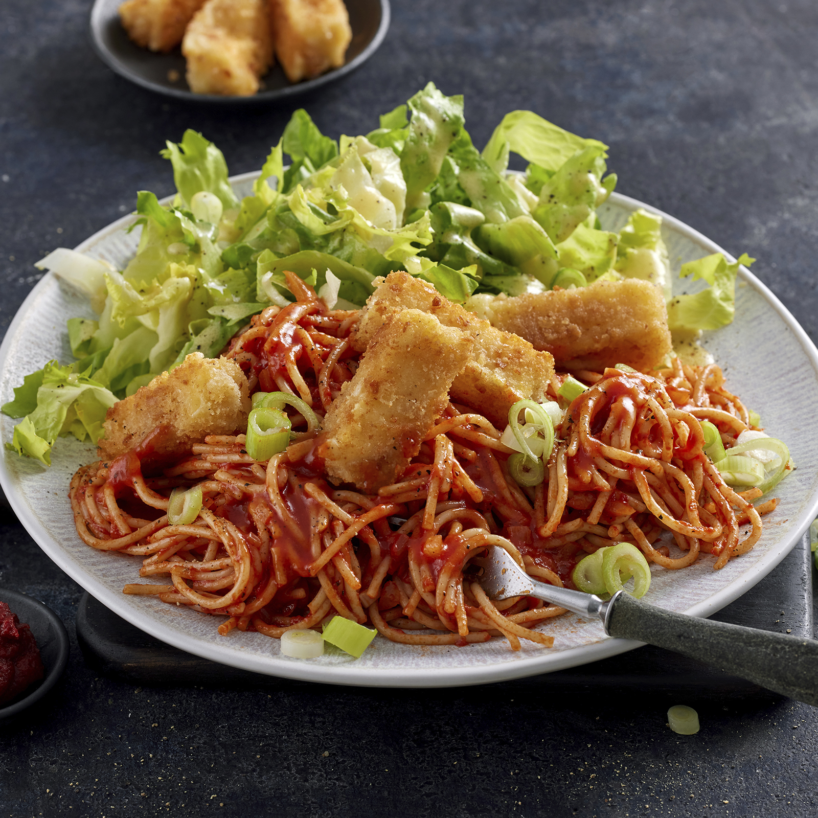 Tomaten-Spaghetti mit Käse-Sticks und Endiviensalat, angerichtet auf einem Teller.